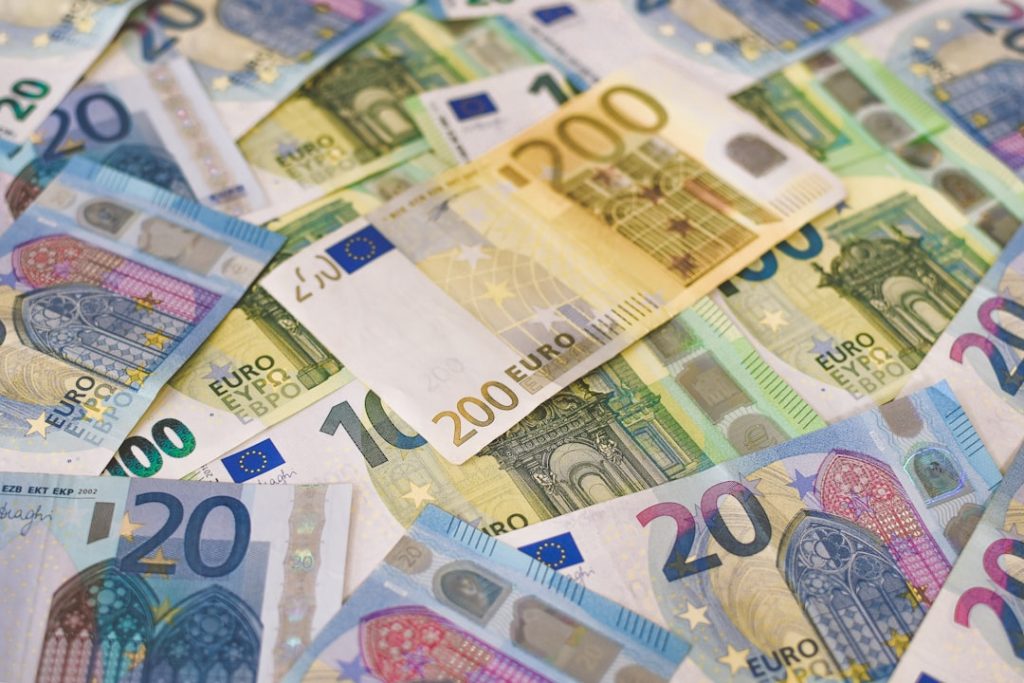 A scattered pile of various euro banknotes, including denominations of 10, 20, 50, 100, and 200 euros, displaying colorful designs and European architectural imagery.