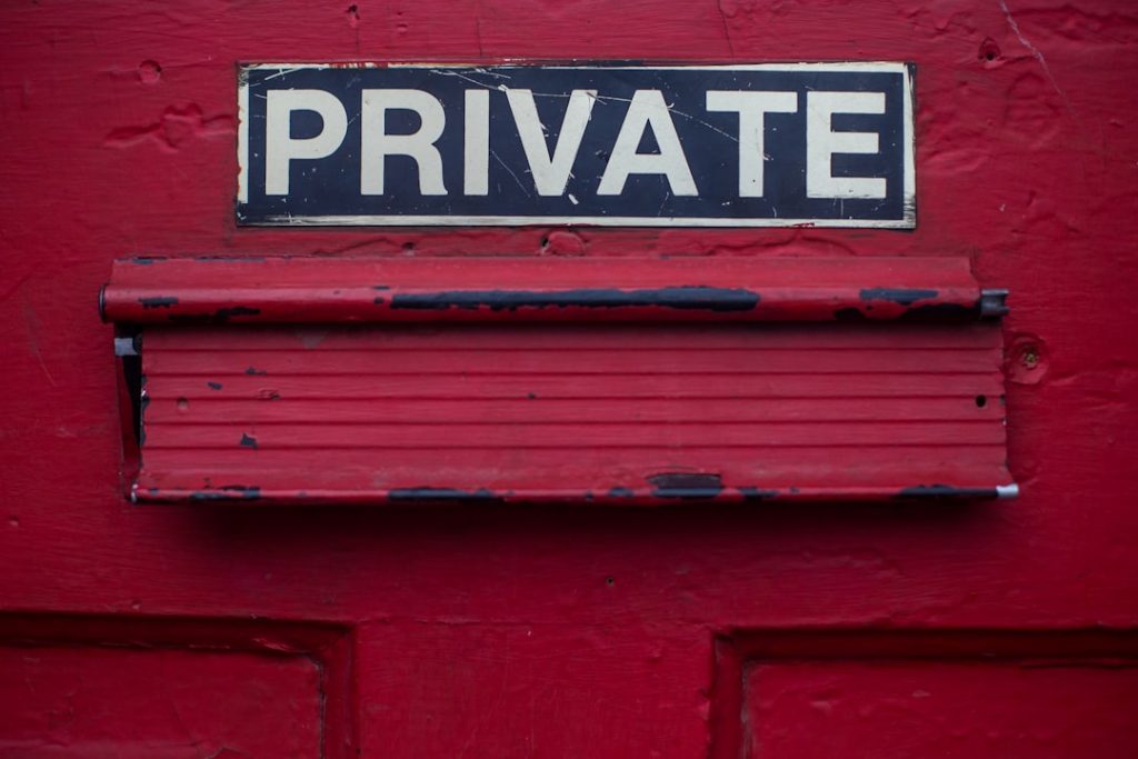 A weathered red door with a black and white sign that reads PRIVATE above a worn rectangular mail slot.