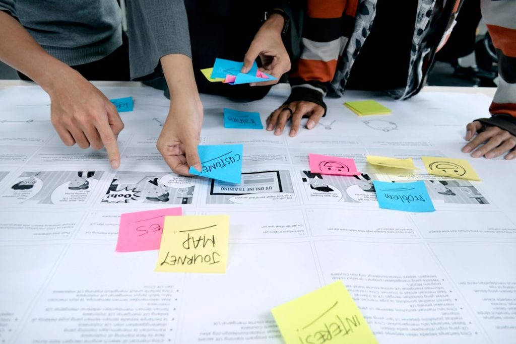 Three people are arranging colorful sticky notes labeled with words like customer, problem, and journey map on a large sheet of printed paper, collaborating on a planning or brainstorming session.