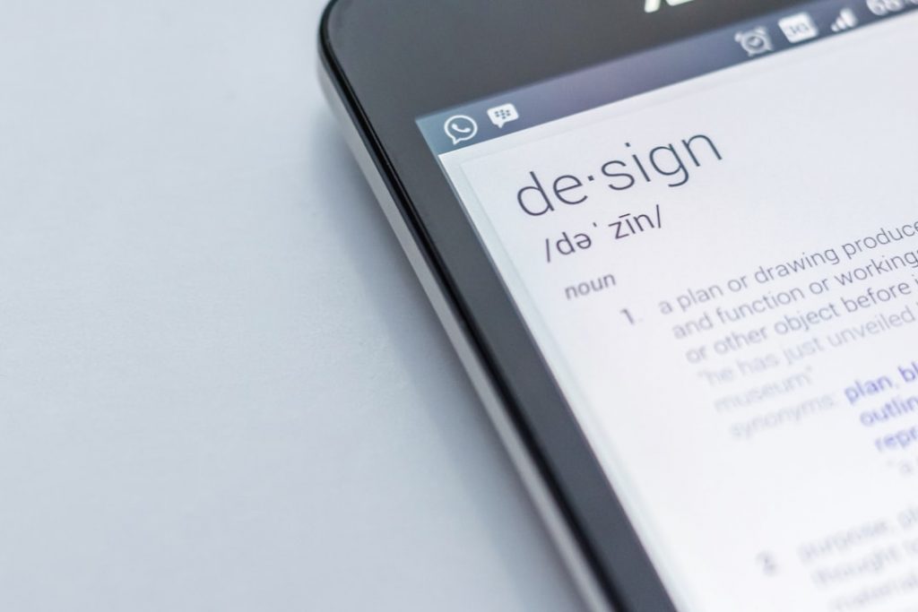 A smartphone screen displays the definition of the word design, showing its pronunciation and part of the meaning, on a white background.