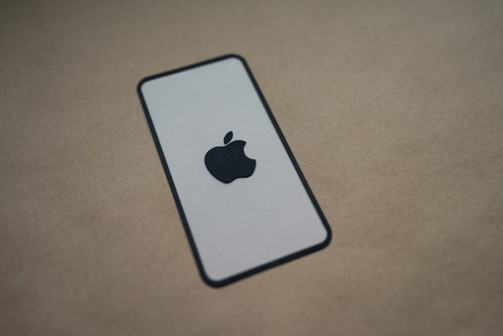A black Apple logo is centered on a white rectangular card with rounded corners, outlined in black, placed on a brown textured surface.