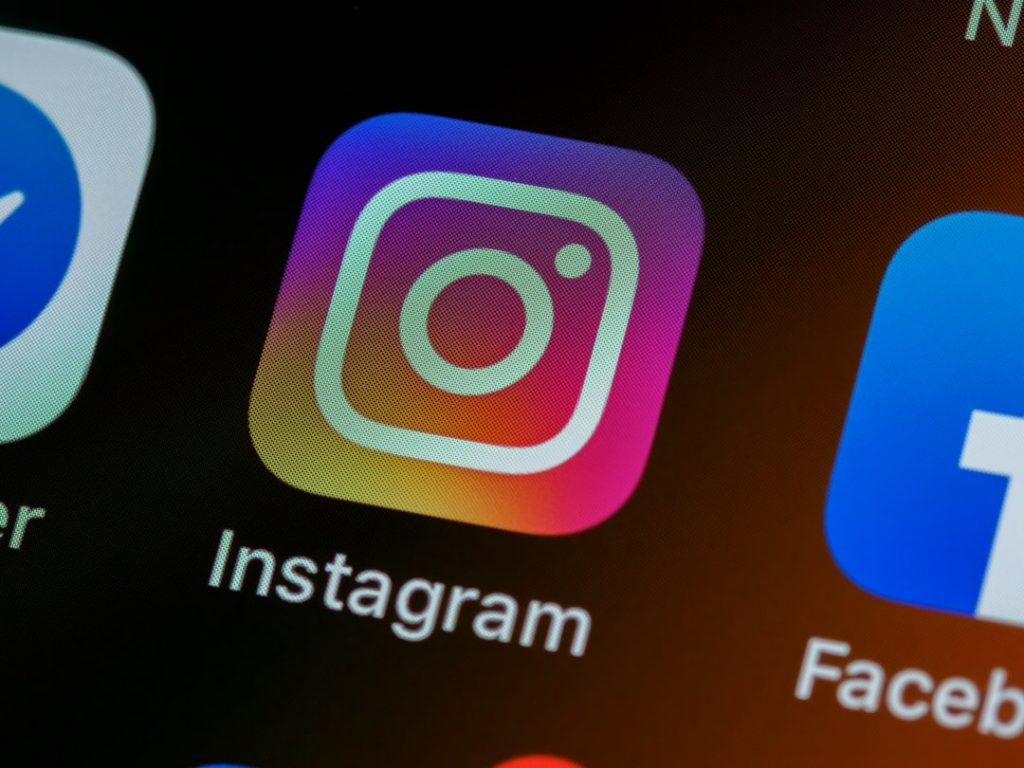 Close-up of a smartphone screen showing the Instagram app icon with a colorful gradient background, and part of the Facebook app icon next to it.