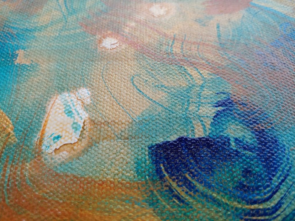 Close-up of a textured canvas with abstract brushstrokes in blue, teal, orange, and white, showing visible paint layers, swirls, and a few worn or chipped areas.