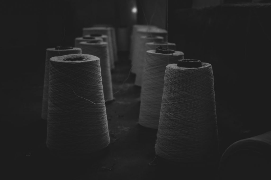 Several large spools of white thread are arranged in rows on a dark surface in a dimly lit room, casting soft shadows around them.